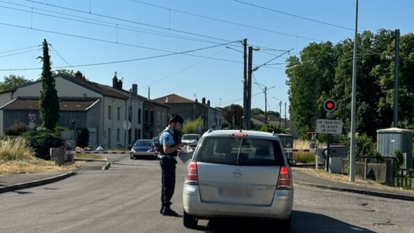 Un gendarme, vu de profil, dispense des conseils de pr&eacute;vention au conducteur d'un v&eacute;hicule gris arr&ecirc;t&eacute; &agrave; un passage &agrave; niveau, dont les barri&egrave;res sont baiss&eacute;es. Au second plan, plusieurs v&eacute;hicules attendent de l'autre c&ocirc;t&eacute; du passage &agrave; niveau.