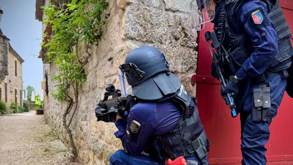 Deux gendarmes équipés en gilet lourd et avec des armes fictives rouge arrivent à un coin de mur, le premier est un genou en terre, son camarade le suit debout