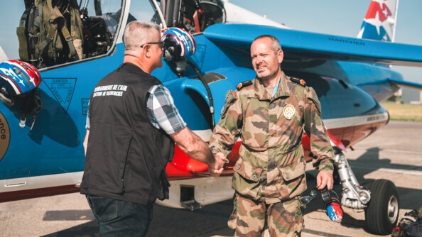 Devant un avion tricolore de la Patrouille de France, un enquêteur de la S.R.  de la G-Air, à gauche, serre la main d'un militaire de la PAF, en treillis, vu de face