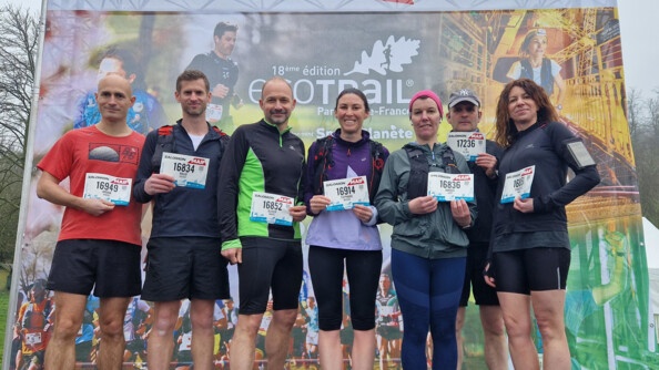 Sept sportifs devant un panneau de l'ecotrail de Paris, portant leur dossards devant eux
