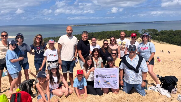 25 personnes dont de nombreux enfants, dans la sable en haut de la dune du pylat, portant la bannière des képis pescalunes