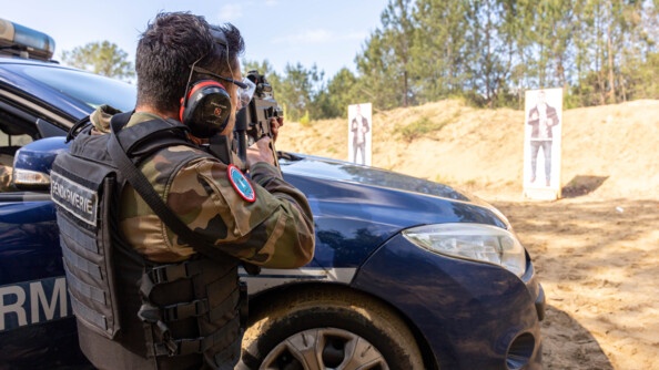 Gendarme se protégeant derrière un véhicule.