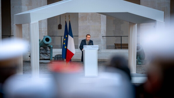 Photo de S&eacute;bastien Lecornu, ministre des Arm&eacute;es et des Anciens combattants, pronon&ccedil;ant son discours, &agrave; l'occasion de la c&eacute;r&eacute;monie de voeux 2025, dans la cour de l'h&ocirc;tel national des Invalides. Le ministre se tient derri&egrave;re un pupitre, sous un auvent, devant un canon. derri&egrave;re lui sont dress&eacute;s les drapeaux fran&ccedil;ais et europ&eacute;en.