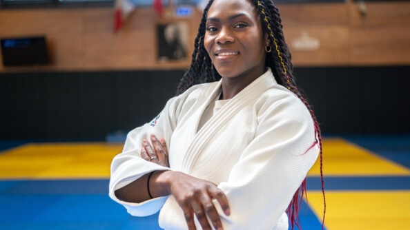 Portrait de la judokate Clarisse Agbégnénou en kimono devant des tatamis.