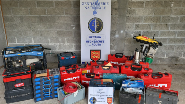 De l'outillage volé saisi par les enquêteurs posé sur le sol d'un hangar, avec en arrière-plan, un kakémono de la section de recherches de Rouen.