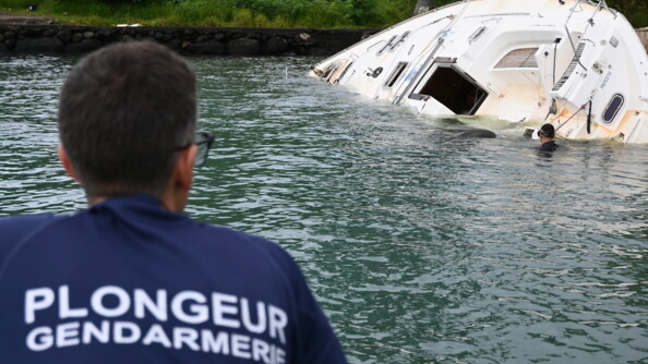 Un plongeur de la gendarmerie de dos  observe l'&eacute;pave d'un voilier &agrave;moiti&eacute; immerg&eacute;e.