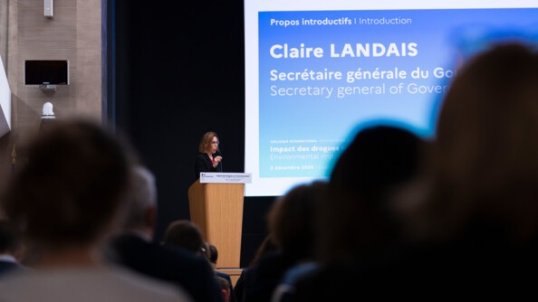 Photo de Claire Landais qui intervient lors d'un colloque. La secr&eacute;taire d'Etat du gouvernement s'exprime au micro devant l'assembl&eacute;e, debout derri&egrave;re un pupitre en bois.