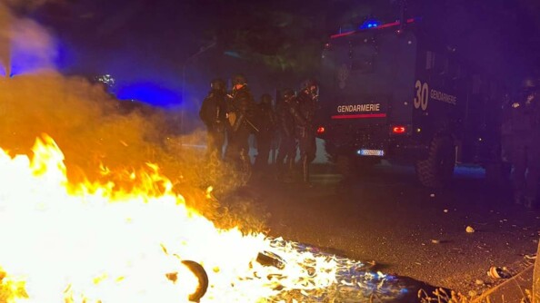 Un feu se propage au premier plan tandis que les gendarmes mobiles sont postés derrière un véhicule Centaure en arrière plan.