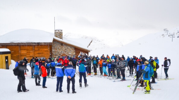 Devant un châlet sur la gauche, une soixantained personnes à skis rassemblées autour de 3 gendarmes