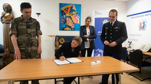 Gaëlle Edon, assise à une table, en train de signer son contrat de sportive de haut niveau de la défense-gendarmerie, entourée d'un général en treillis à gauche et d'un général en vareuse à droite.