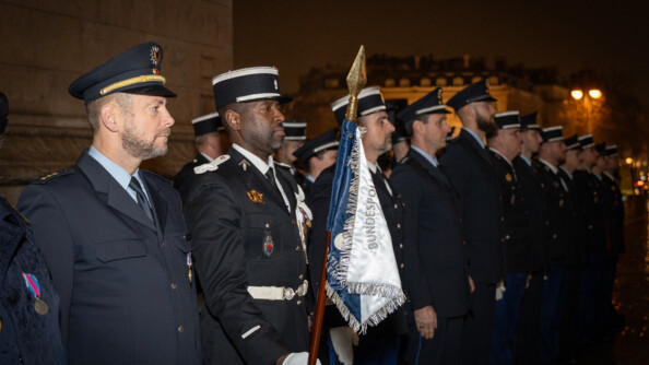 Des gendarmes fran&ccedil;ais et policiers allemands en rang dans la ville de nuit &eacute;clair&eacute;e. le premier gendarme vers la gauche tient dans sa main droite le fanion de l'unit&eacute;, bleu et blanc