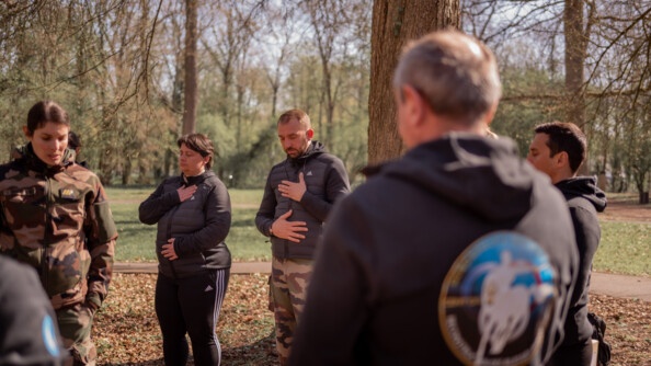 Exercice de relaxation en forêt lors d'une séance ORFA (Optimisation des ressources des forces armées). Les participants ont les yeux fermés et les deux mains posées sur le ventre et la poitrine.