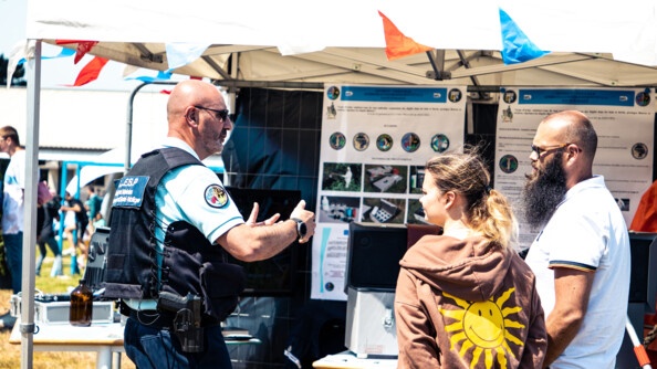 Un gendarme échange avec deux visiteurs devant un stand.