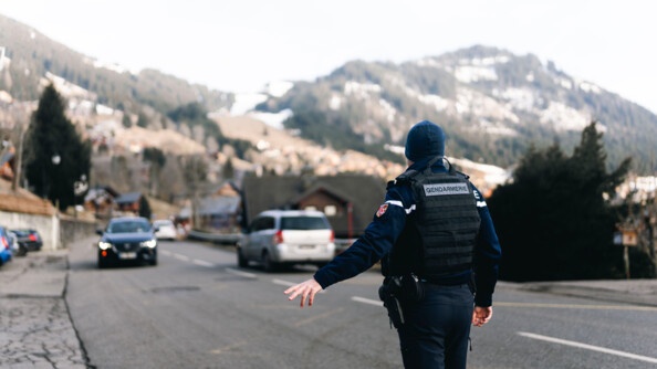 Un gendarme, debout sur la chaussée, sur la commune de Châtel, en Haute-Savoie, fait un signe de la main gauche, invitant un automobiliste conduisant un véhicule de couleur noire, à s'arrêter sur le bas côté, pour pouvoir procéder à un contrôle.