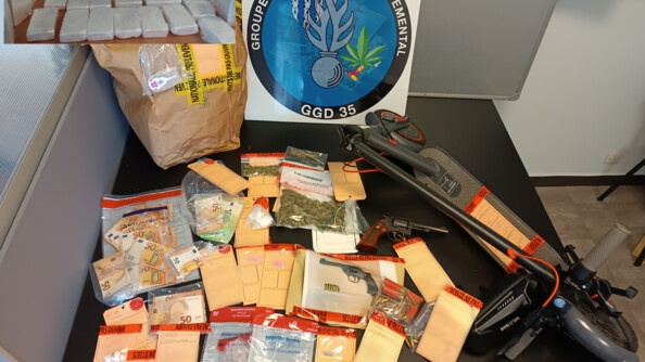 Tous les scellés (argent, cachets, armes, trottinette) posés sur une table, avec en fond la rondache du GSD. En incrustation, une photo représentant plusieurs paquets de poudre blanche (kétamine) posés sur une table.