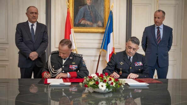 Deux militaires en train de signer des documents sur une table e marbre gris recovert d'un bouquet blanc et rouge. Derrière eux deux hommes en costard et les drapeaux français et monégasques autour d'un portrait ancien d'un religieux
