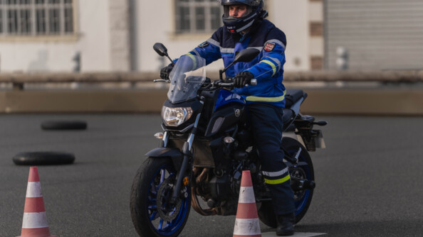 Un motard de la gendarmerie sur sa moto en attente entre deux plots orange et blancs, derrière une ligne jaune, sur un plateau de moto