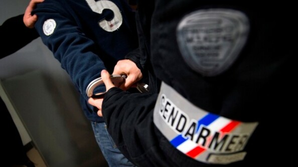 Un gendarme dont on ne voit que le brassard est entrain de menotter un individu.