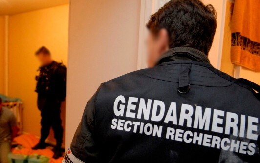 Enquêteur d'une section de recherches vu de dos. Au second plan un second gendarme surveille un individu interpellé à genou.