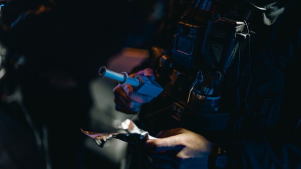 Focus sur les mains du gendarmes en train de regarder un alcootest et les papiers du véhicule qu'il controle. Il fait nuit et sombre.