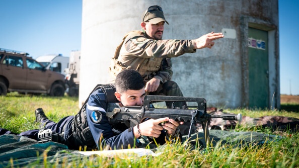 Un gendarme couché au sol dans l'herbe, armé d'un fusil, en train de viser. A ses côtés, un militaire de l'armée de terre accroupi désigne une cible.