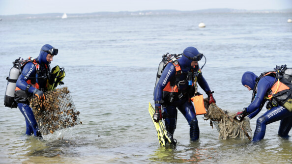 Trois plongeurs de la gendarmerie sortent des filets de déchets de l'eau