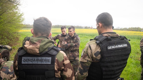 Des officiers-élèves au premier plan interceptent des miliciens à la lisière de la forêt