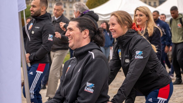 Marjorie Delassus, avec le porteur du drapeau des Jeux Paralympiques, en fauteuil roulant, ils sont souriants et se dirigent vers l'h&ocirc;tel national des invalides