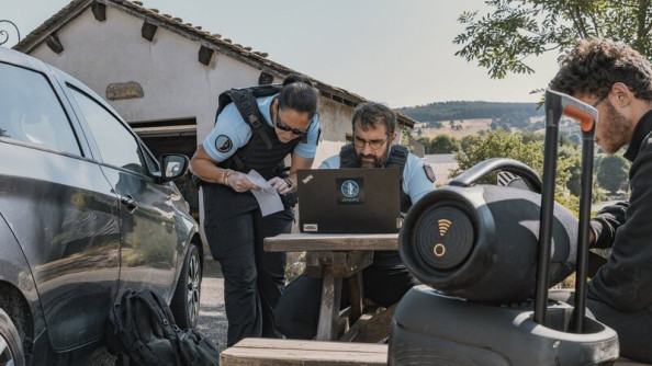 Deux gendarmes consultent un &eacute;cran d'ordinateur, install&eacute; sur une table en bois, dans un village.