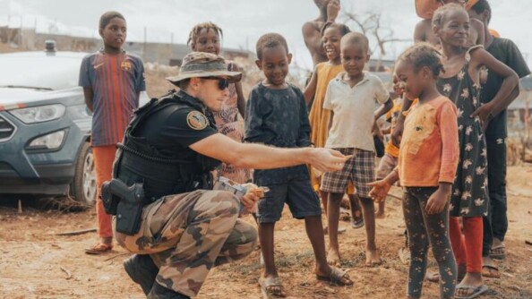 Photo d'un gendarme accroupi, au milieu d'un groupe d'enfants mahorais, tend quelque chose à une fillette, qui regarde la main du militaire en souriant.