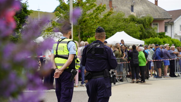 De dos, une gendarme de brigade et u nautre de PSIG attendent sur une route, de nombreuses personnes en sécurité derrière une barrière
