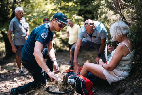 Des gendarmes portent secours à une femme blonde blessée, assise sur le sol, dans un espace boisé.