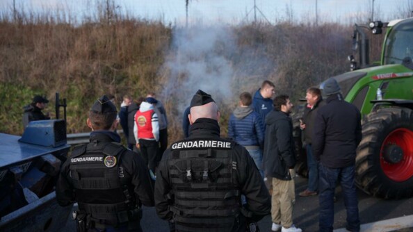 Deux gendarmes mobiles de dos. En fond devant eux, des agricutleurs échangent calmement.