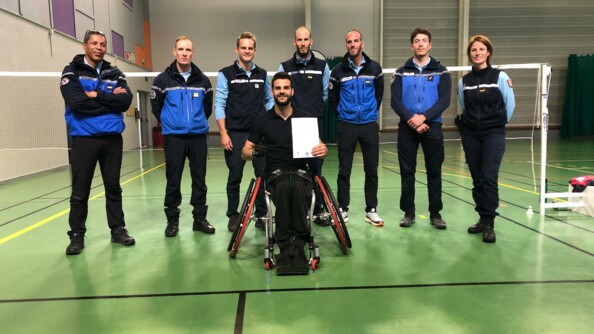 Thomas Jakobs et les militaires du PGHM se tenant devant le filet de badminton apr&egrave;s l'entrainement. Thomas tient la convention dans ses mains.