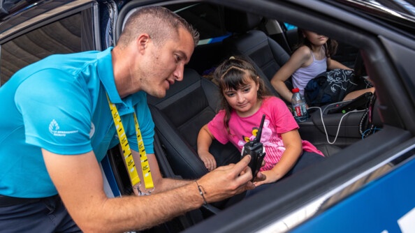 Deux fillettes sont installées à l'avant d'un véhicule. Un gendarme se trouve à leurs côtés, à l'extérieur du véhicule. Il montre un téléphone à l'une des petites filles.