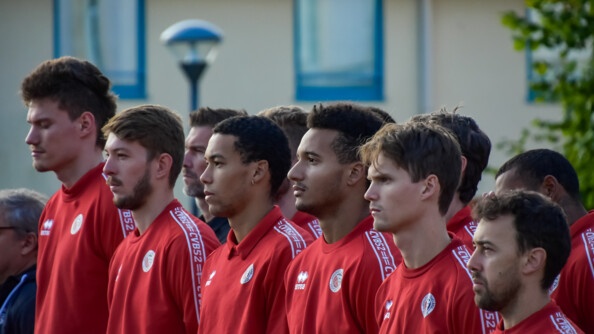 Gros plan sur la première rangée de six sportifs vêtus d'un sweat rouge.