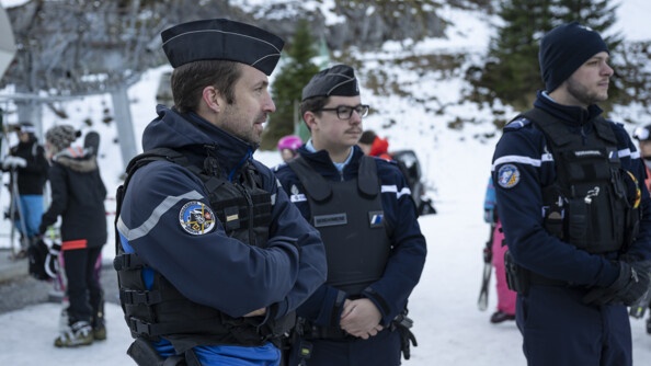 Trois gendarmes devant des familles de skieurs dont un porteur de la rondache "Gendarmerie groupe montagne" sur son bras droit