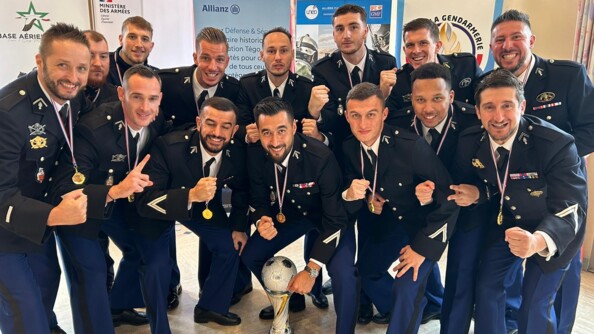 Quatorze militaires souriants, en tenue bleue marine, posent autour d'un trophé de futsal. Ils sont dans une salle fermée. Derrière eux, on aperçoit des pancartes à l'éffigie de la gendarmerie nationale ou encore du ministère des Armées.