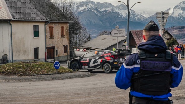 Un gendarme en extérieur, sécurise le passage de la course sur un rond point. Devant lui, l'on voit les alpes du sud.