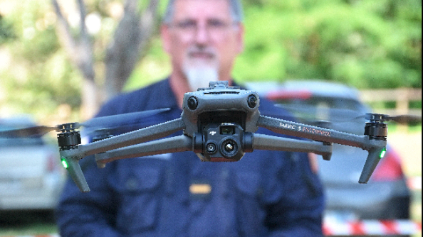 La photo représente un télépilote de drone de la gendarmerie, engagé à l'occasion du festival Garorock 2025. L'homme tient une télécommande de ses deux mains. Au premier plan, sur la photo, apparaît le drone, volant à hauteur du visage du télépilote.