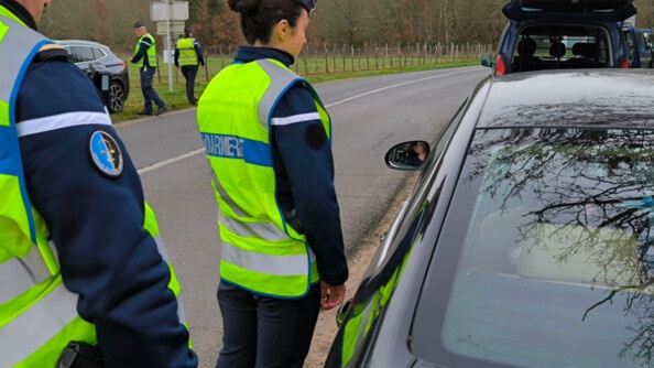Deux gendarmes de dos contrôlant un véhicule sur le bord de la route. Au loin, deux autres gendarmes font de même.