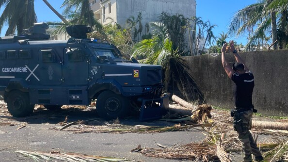 Un gendarme guide un véhicule blindé de la gendarmerie, déblayant une route bloquée par des branches et des troncs d'arbres arrachés, après le passage du cyclone Garance à La Réunion.