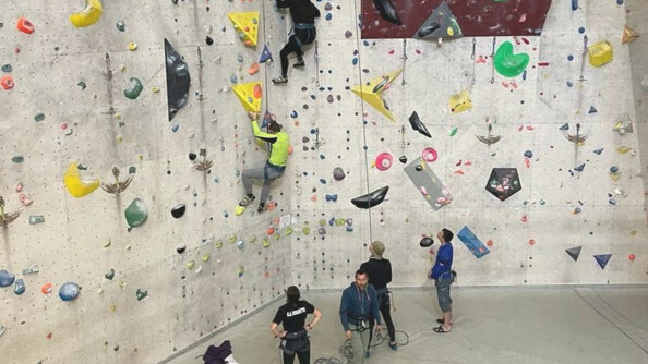 Quatre personnes se tiennent debout au pied d'un mur d'escalade, tandis que deux autres personnes montent le long du mur