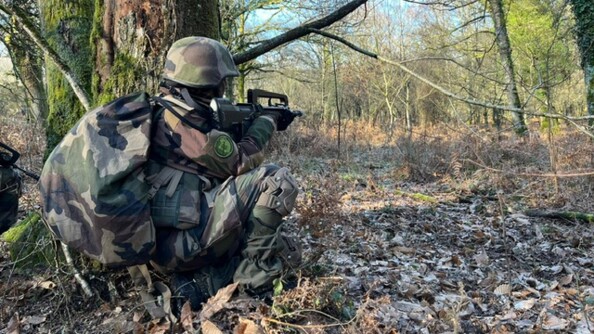 Un gendarme dans la for&ecirc;t en tenue de combat. Il est en entra&icirc;nement. Il se cache derri&egrave;re un arbre tenant dans ses mains un FAMAS.