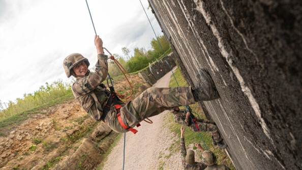 Un élève officier descend en rappel et regarde la caméra en souriant