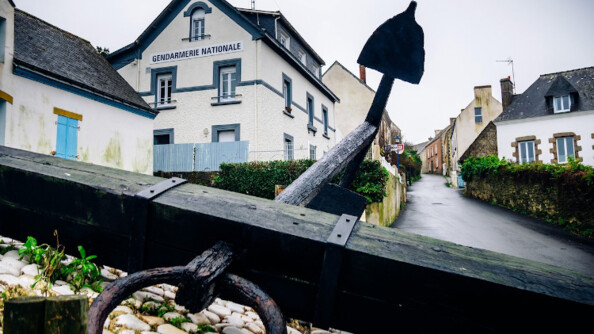 Vue de la brigade de gendarmerie de l'Île de Groix, image en contre-plongée avec au premier plan une ancre de bateau en bois noir