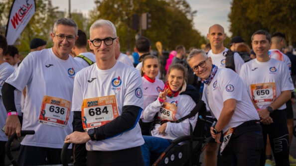 Des coureurs, vêtus d'un T-shirt blanc avec un numéro sur le ventre, posent autour du fauteuil roulant d'une jeune femme souriante, aux cheveux chatains réunis en queue de cheval.