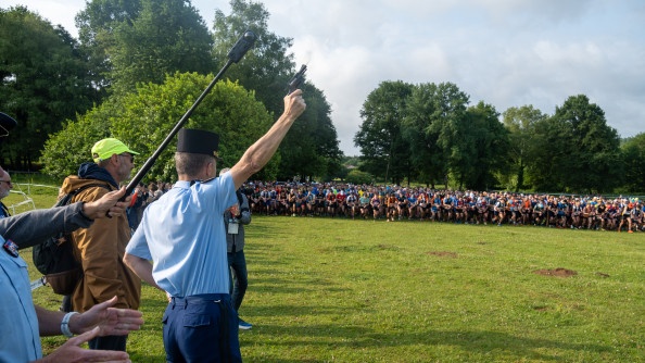 Un général de dos tire un coup en l'air pour lancé la course des 32 km. Au fond, on aperçoit, sur le départ, les courreurs.