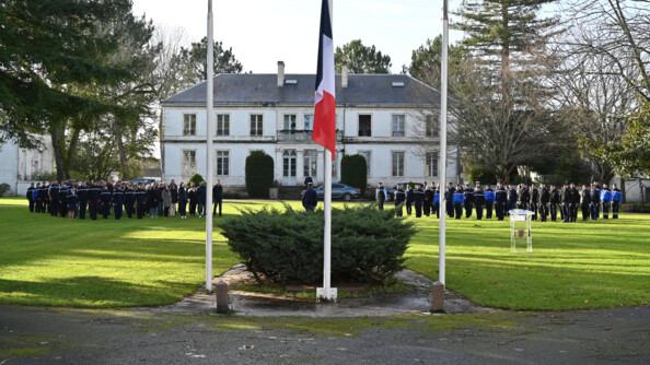 sur une place e herbe des gendarmes et civils alignés, au milieu au premier plan, le drapeau frnaçais