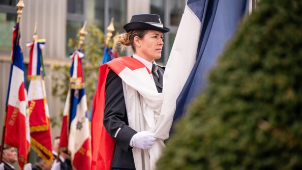 Une gendarme tient un dapeau français avant le lever des couleurs.